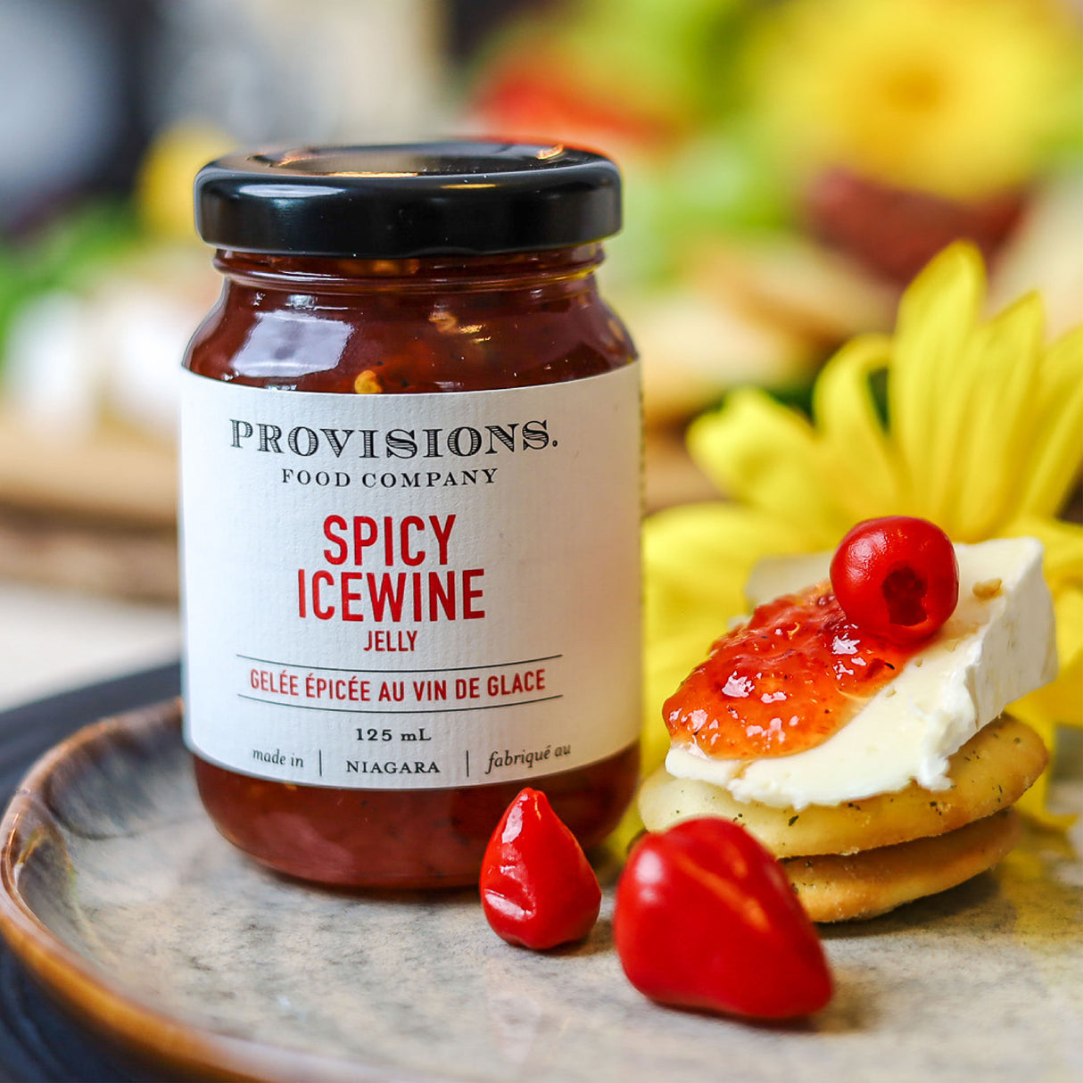 Provisions Spicy Icewine Jelly on charcuterie board with a slice of brie cheese and pickled hot peppers.