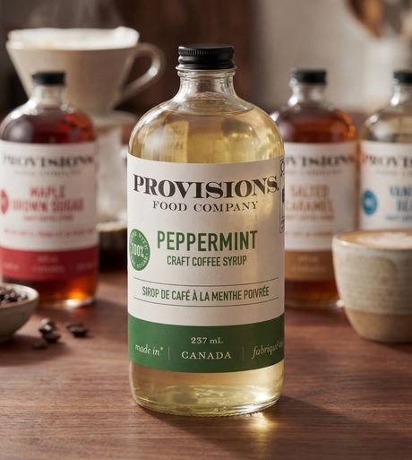 Bottle of Provisions Food Company peppermint craft coffee syrup on a wooden surface with coffee-related items in the background.