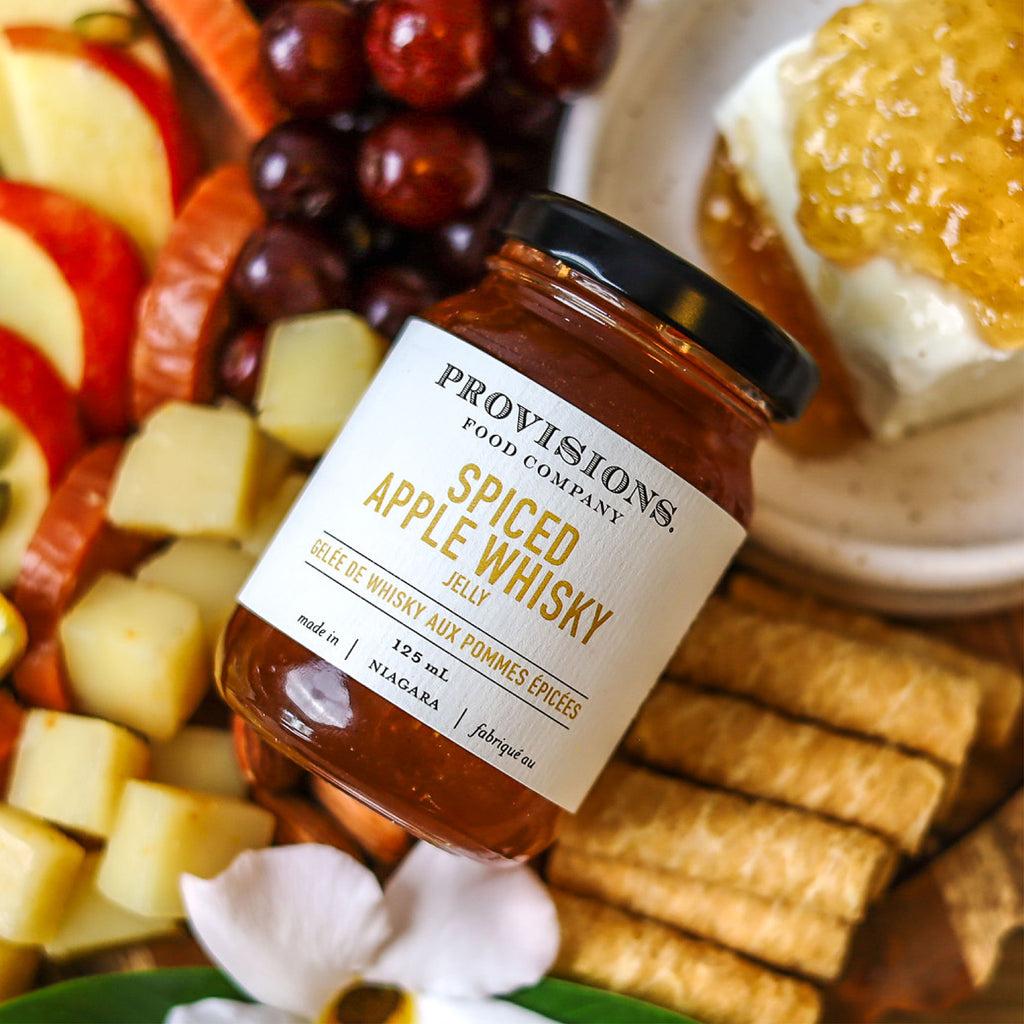 Provisions Spiced Apple Whiskey Jelly resting on a colourful charcuterie board.